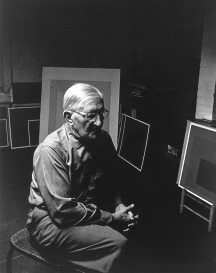 Portrait de Josef Albers assis dans son atelier de peinture avec ses tableaux "hommage au carré"